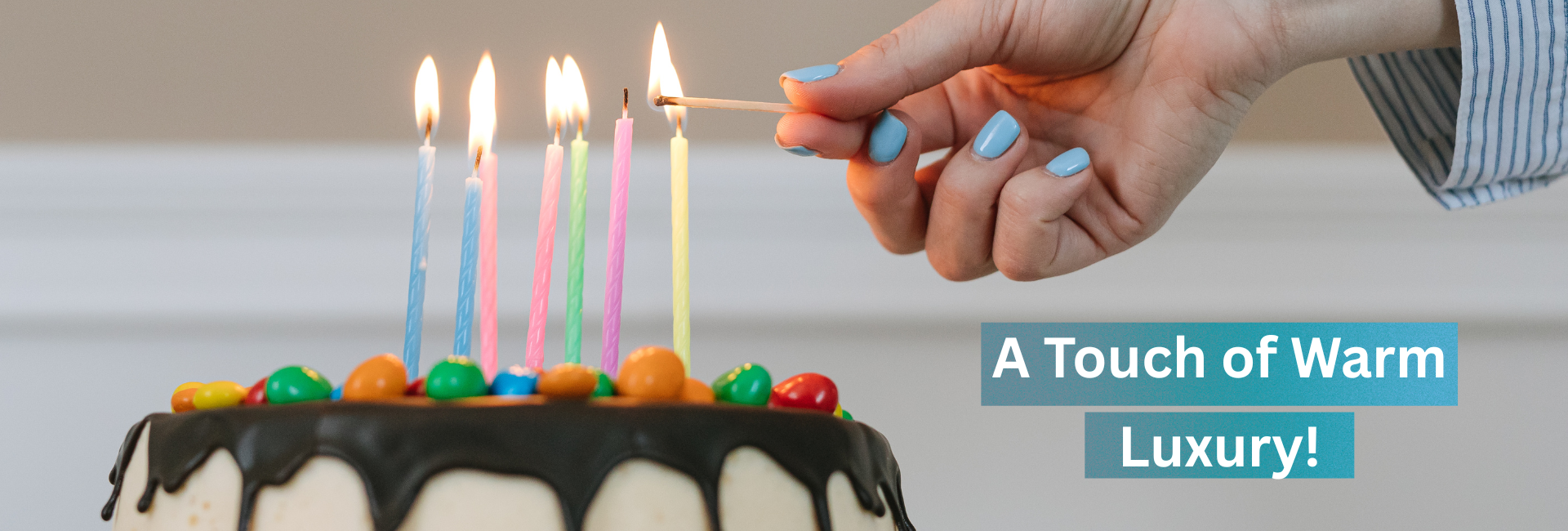 Someone with light blue nailpolish is lighting up thin candles on a chocolate topped cake - the writing says A touch of Warm Luxury